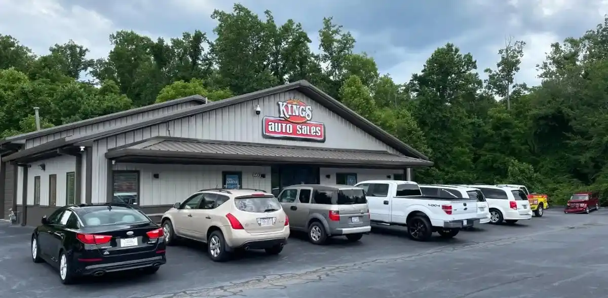 Front view of Kings Auto Sales storefront with a row of parked cars in the lot and a sign on the building reading 'Kings Auto Sales'